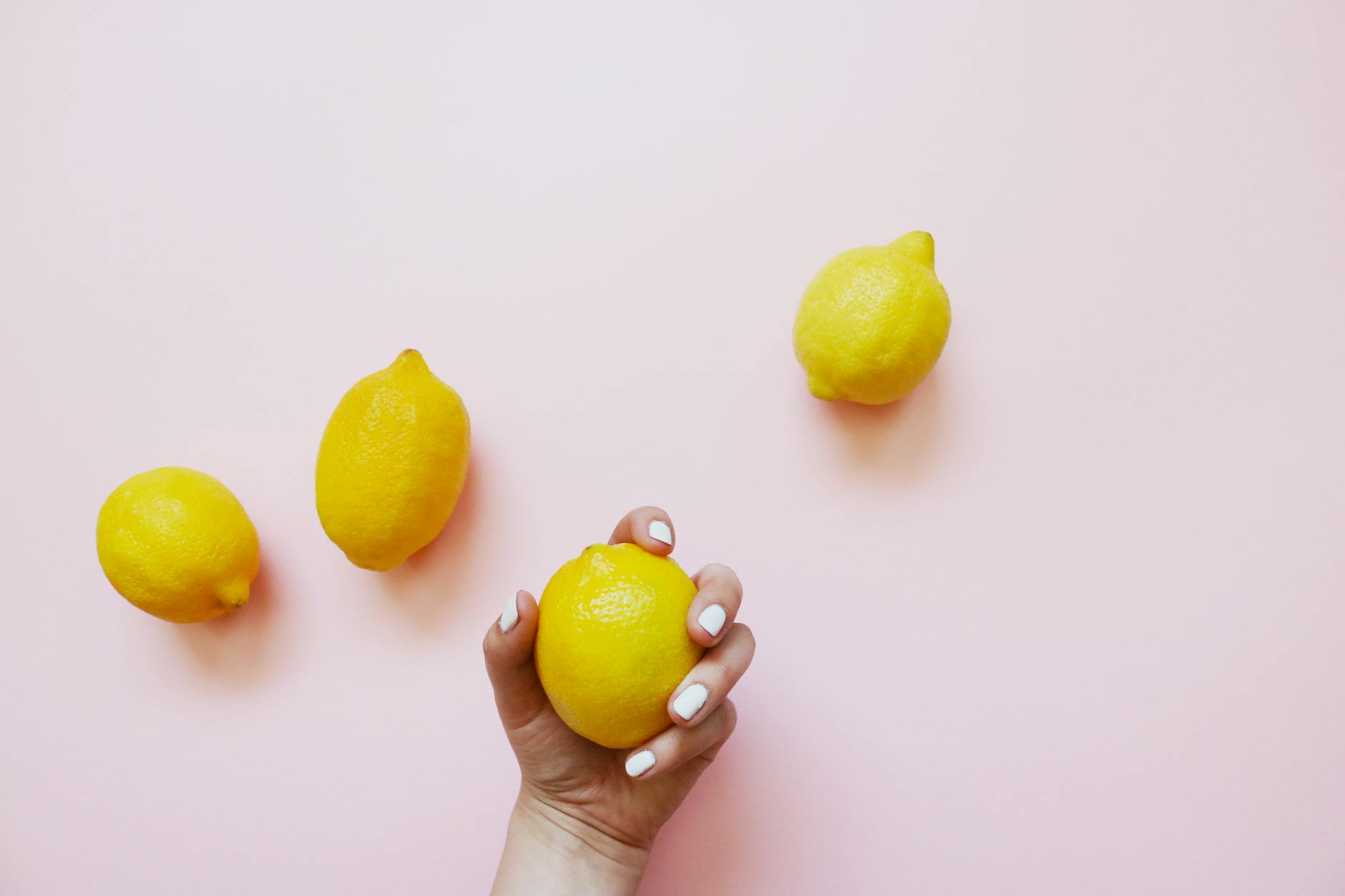 Hand holding a lemon on a soft pink background, representing reconnection and sensuality