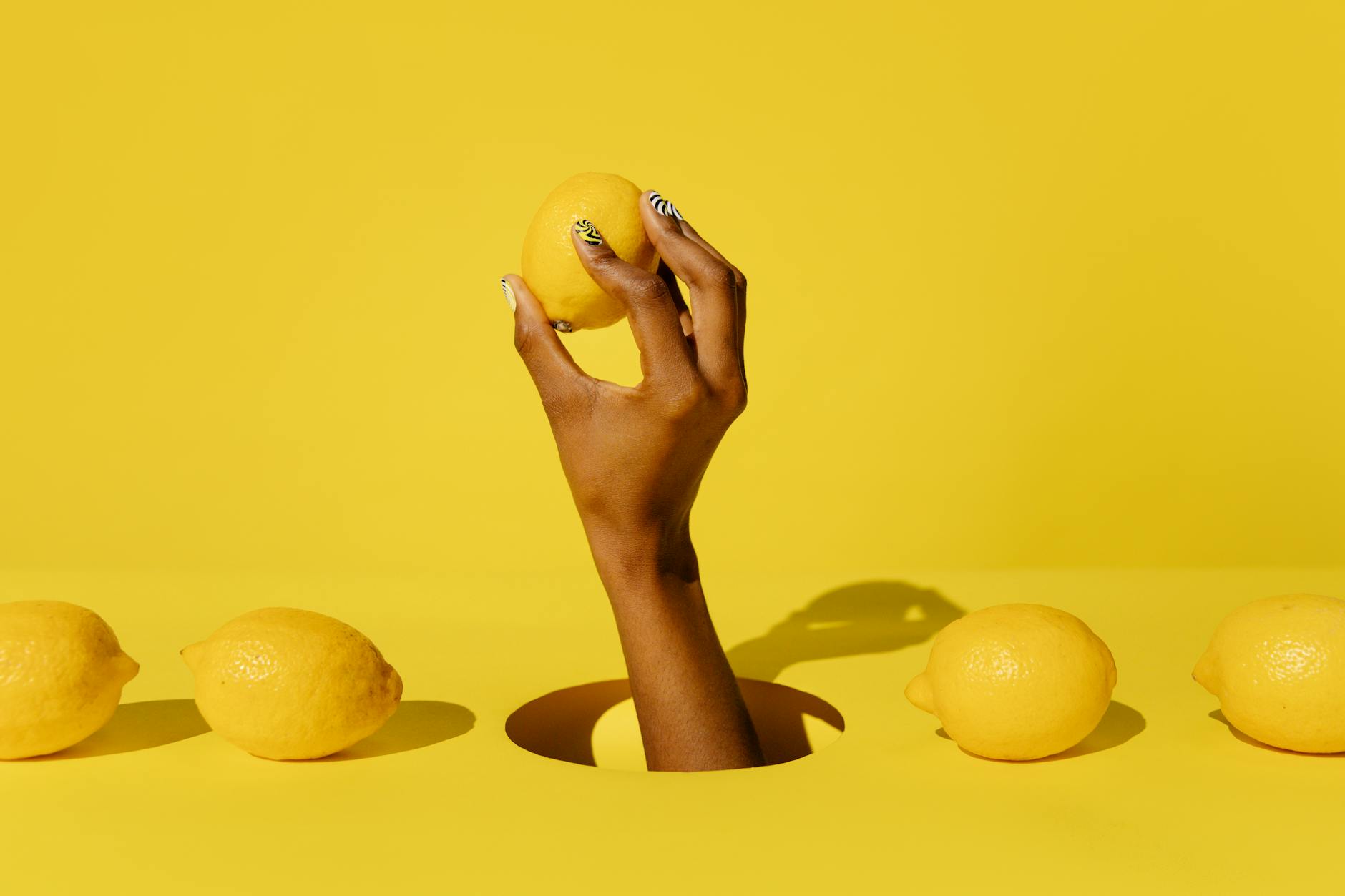 Two hands holding pink and blue Lemon clitoral vibrators against a pastel background