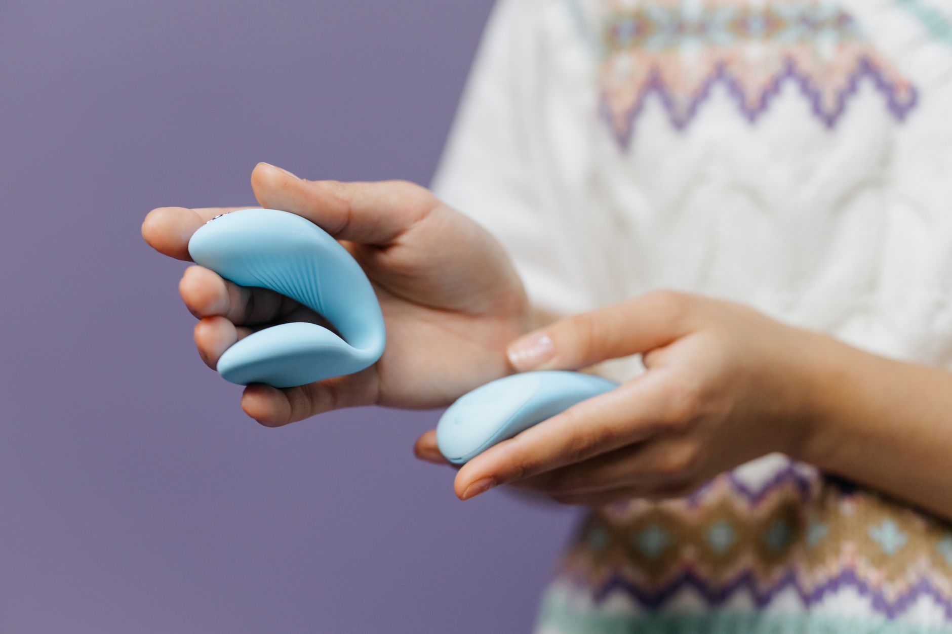 Close-up of hands holding a sleek blue vibrator against a purple background, symbolizing post-surgery intimacy recovery