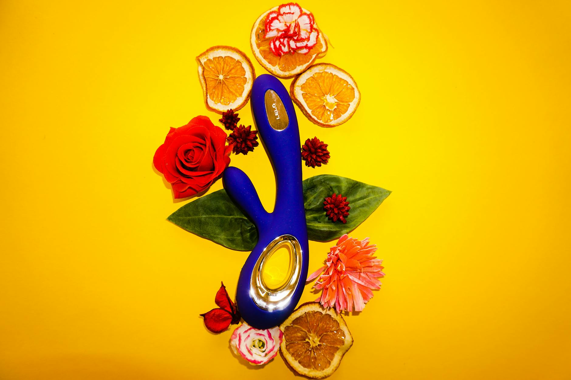 A blue vibrator surrounded by fresh lemons and citrus slices on a bright yellow surface