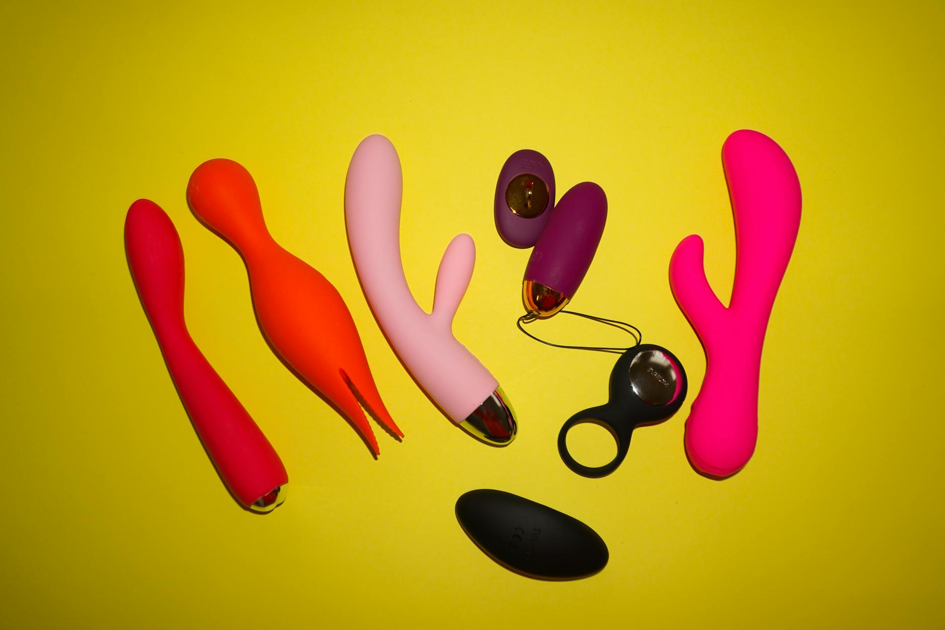 Colorful sex toys arranged on a bright yellow background, representing sexual wellness and pleasure tools